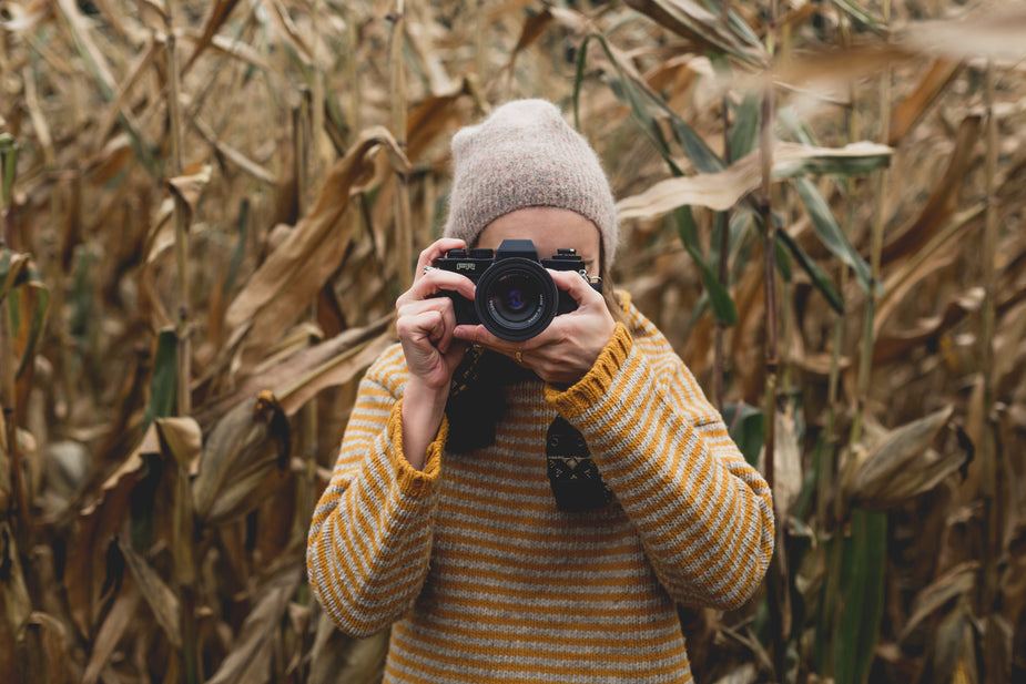 Person wearing yellow wool jumper with wide sleeves and thick cuffs taking photo in autumn field