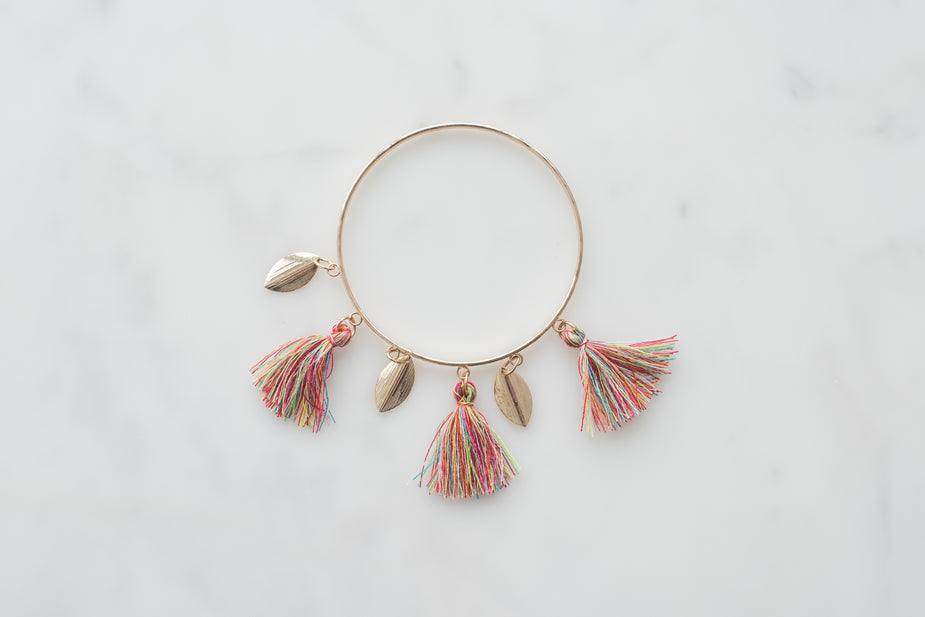 Gold boho bangle bracelet with multicolor tassels and charms on white background