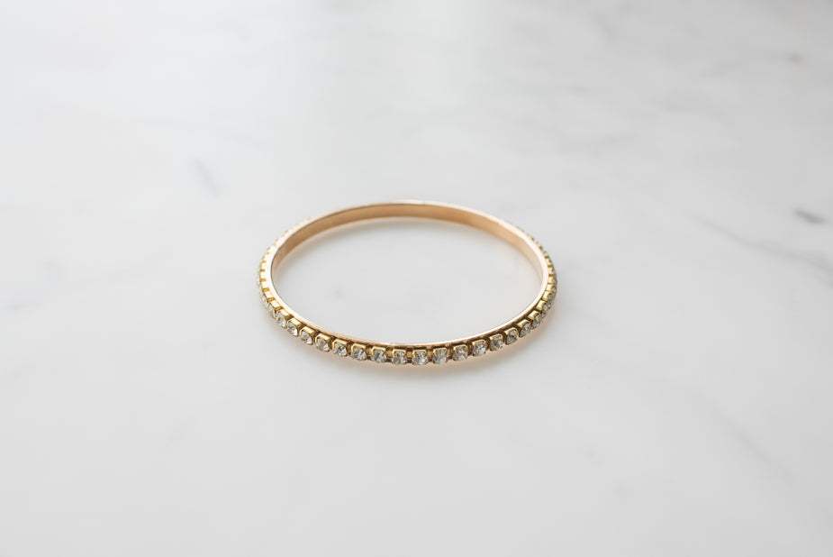 Gold bangle bracelet studded with jewels on marble background