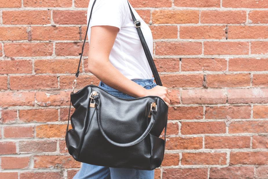 Woman carrying black leather bag over shoulder against brick wall background