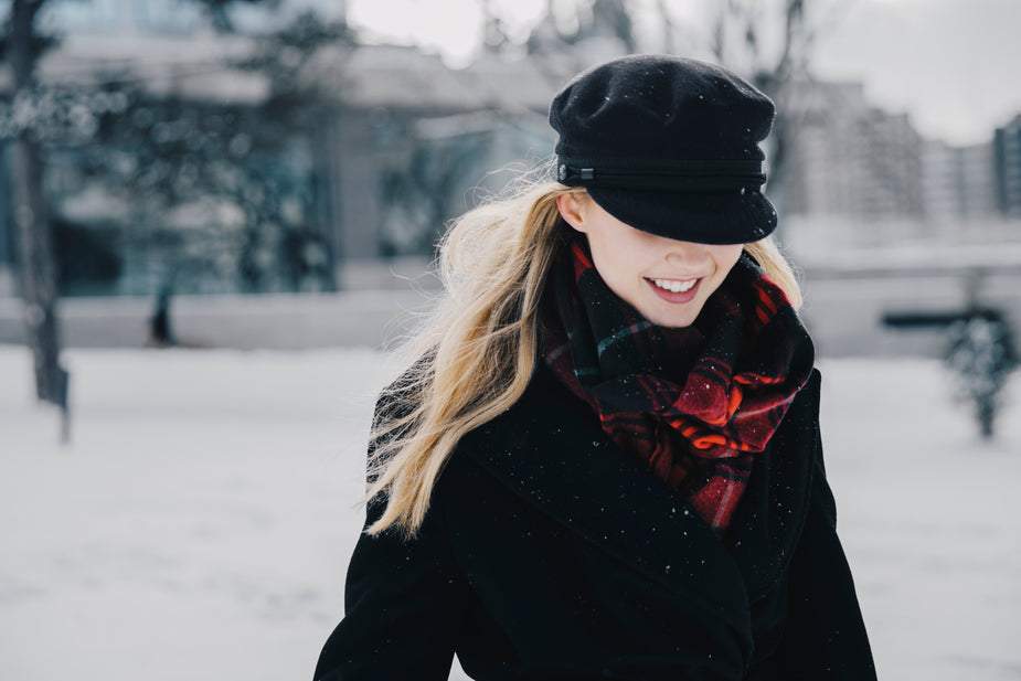 Woman wearing black soft winter jacket with fleece lining and red plaid scarf in snowy outdoor setting
