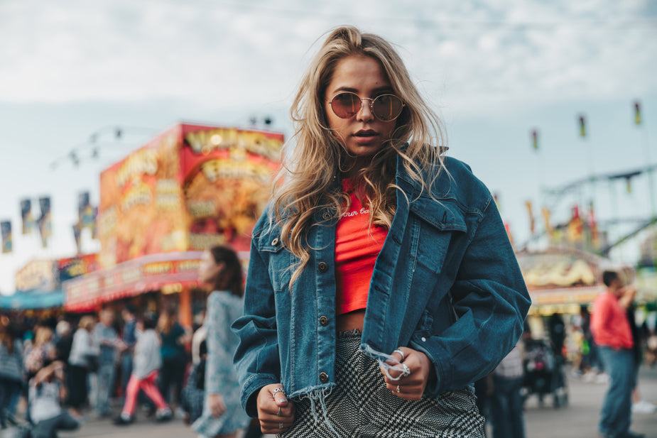 Woman wearing a classic dark denim top with chest pockets, buttoned cuffs, and ripped hem, styled at an outdoor fair.