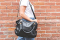 Woman carrying black leather bag over shoulder against brick wall background