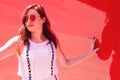 Woman wearing sleeveless floral white top with black floral patterns and sunglasses against red background