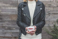 Woman wearing classic black leather jacket with front zipper and quilted shoulder pads holding a cup