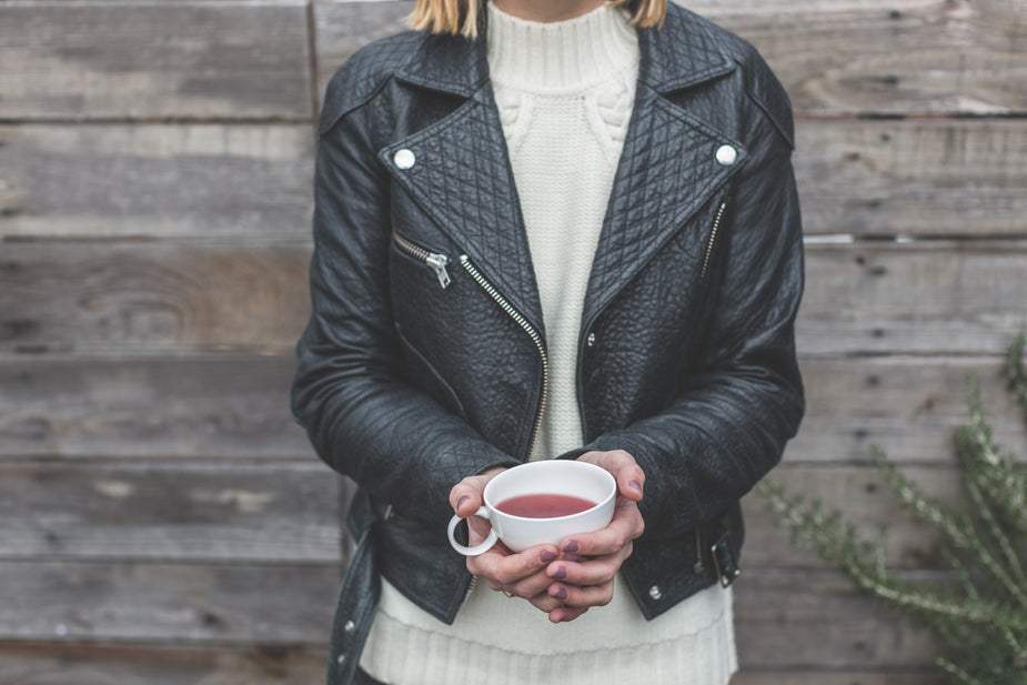 Woman wearing classic black leather jacket with front zipper and quilted shoulder pads holding a cup