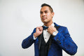 Man adjusting bow tie wearing blue silk tuxedo with marbled aquatic pattern and black buttons