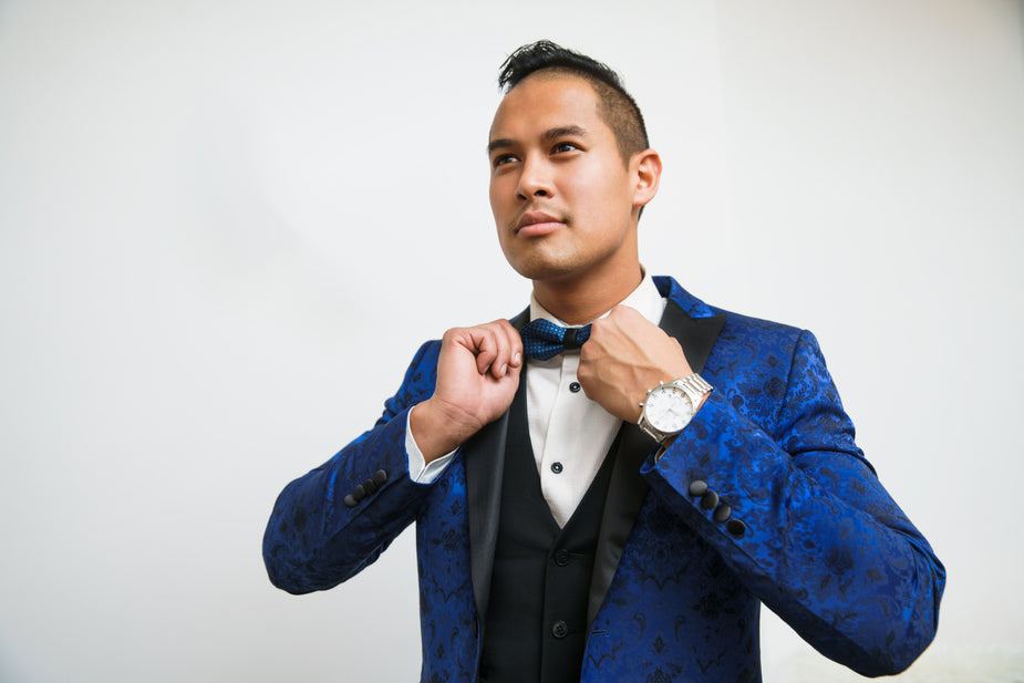 Man adjusting bow tie wearing blue silk tuxedo with marbled aquatic pattern and black buttons