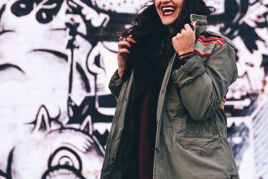Woman wearing loose fitting olive green jacket with buttons and multicoloured shoulder pattern
